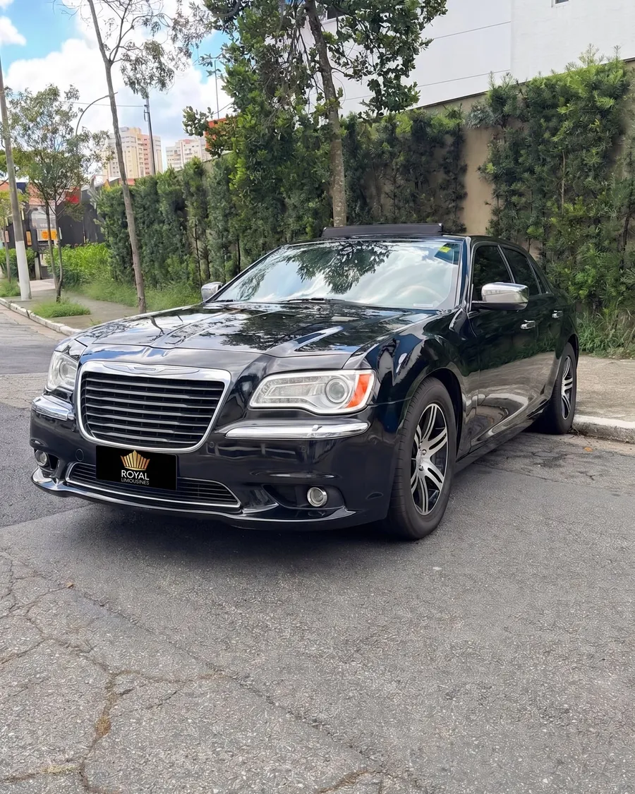 Chrysler 300C preto visto de frente em três quartos, estacionado em uma rua residencial