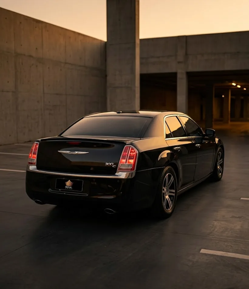 Chrysler 300C preto visto de trás em três quartos, estacionado em uma garagem de concreto ao fim da tarde