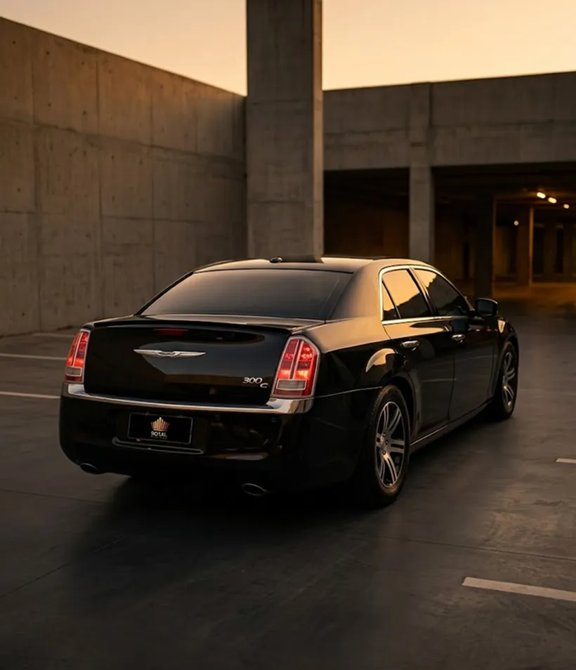 Chrysler 300C preto visto de trás em três quartos, estacionado em uma garagem de concreto ao fim da tarde